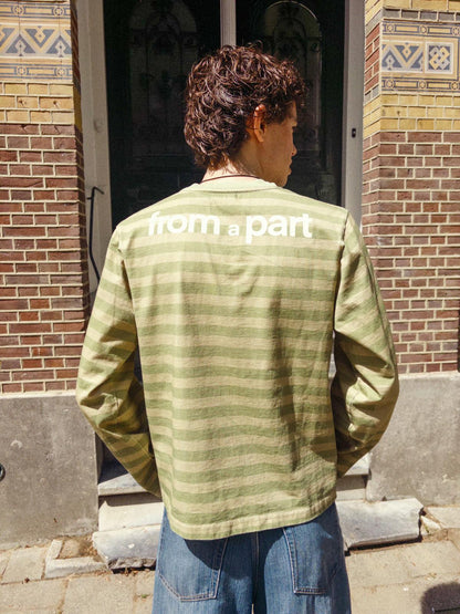 Person wearing a green shirt with 'from part' text on the back, standing in front of a brick building.